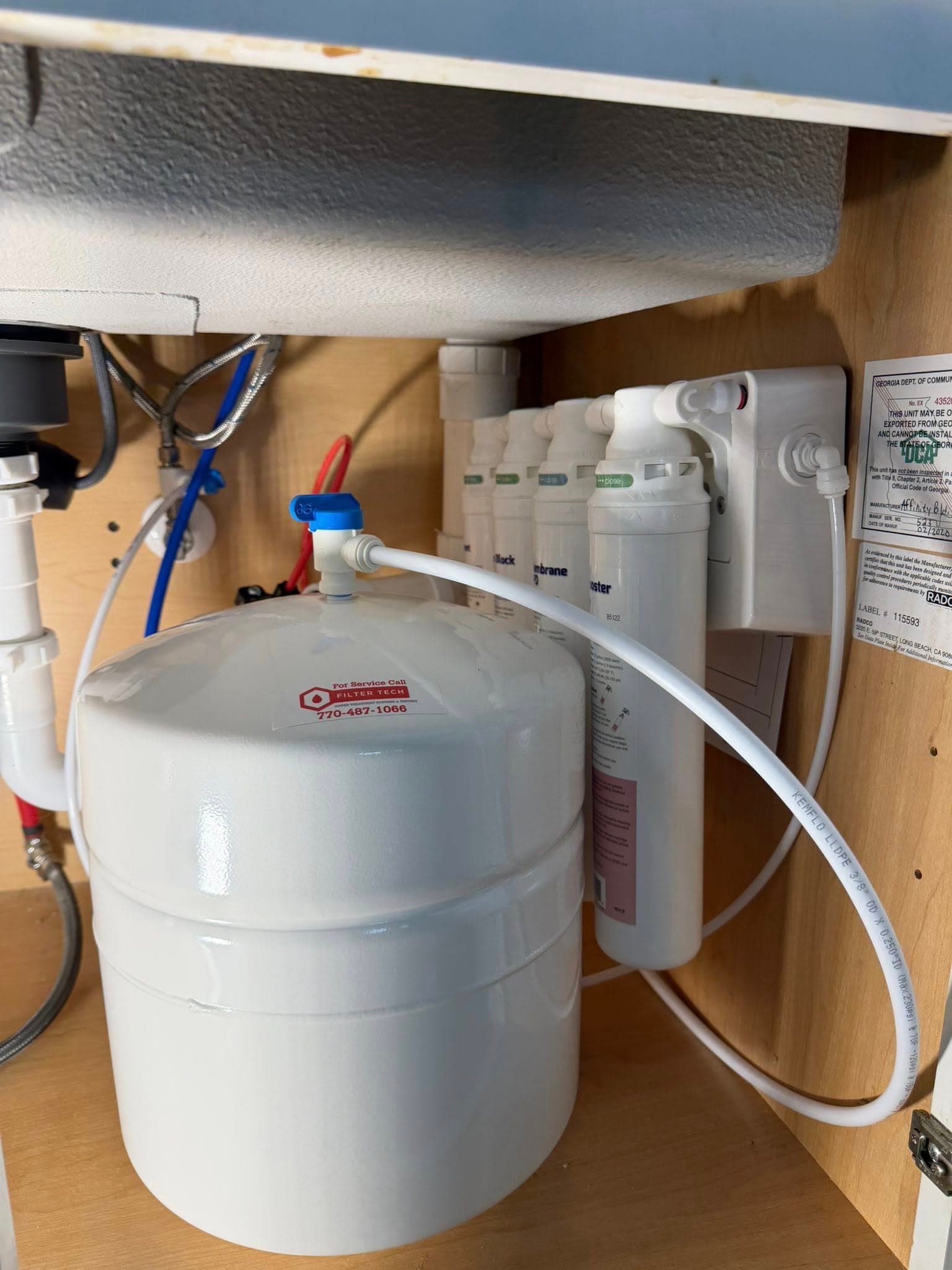 A Filter Tech reverse osmosis system installed under a kitchen sink — storage tank, multi-stage filters, and dedicated faucet line