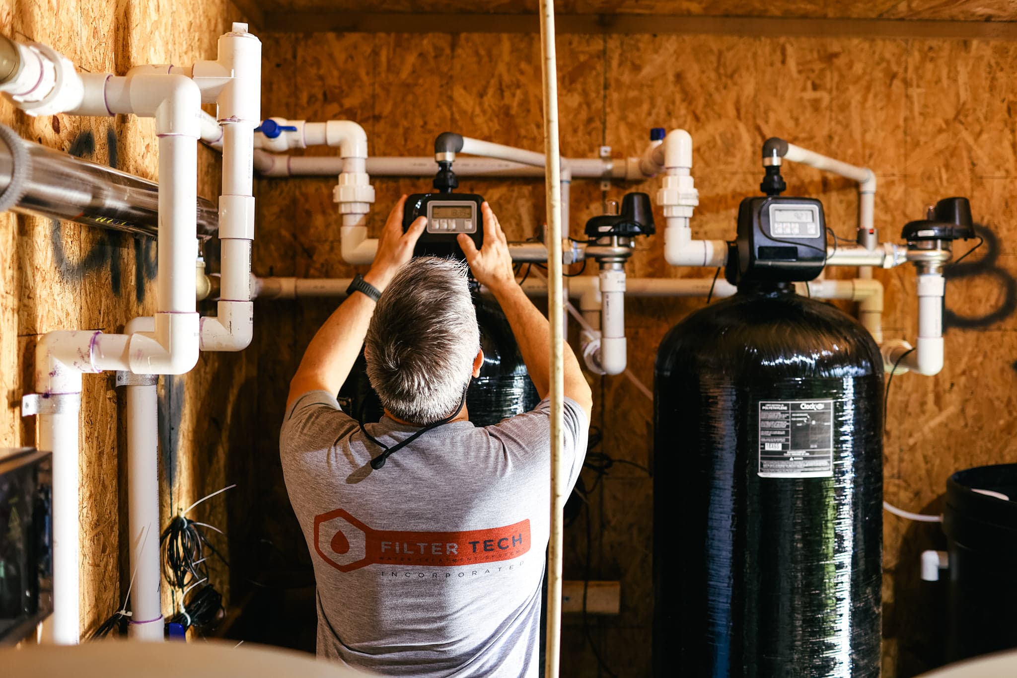 Jay Hanlon installing a whole-house filtration system — adjusting the control valve above the filter tanks